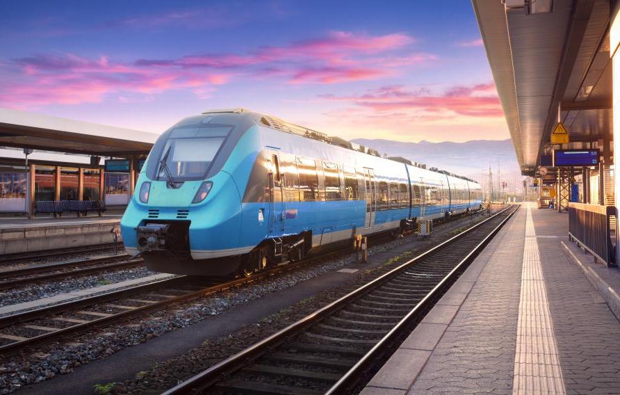 Stock image of a blue passenger train on tracks with pink and purple sunset